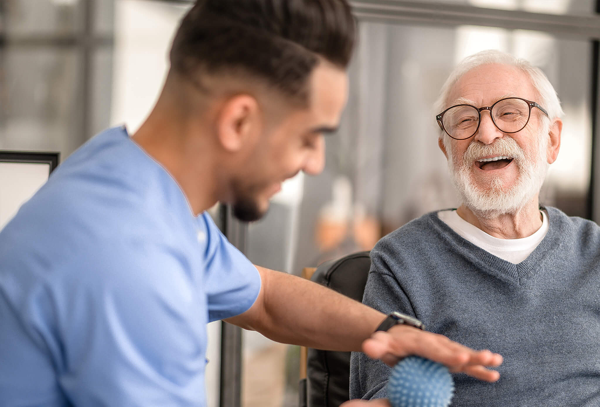 Pflegekraft demonstriert Bewegungsübungen mit älterem Patienten