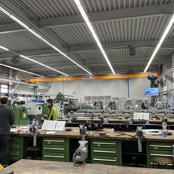 Viele Mitarbeitende arbeiten konzentriert an Maschinen und Werkbänken in heller Umgebung