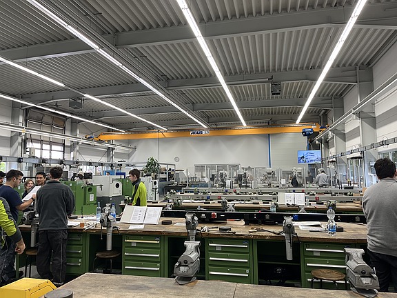 Viele Mitarbeitende arbeiten konzentriert an Maschinen und Werkbänken in heller Umgebung