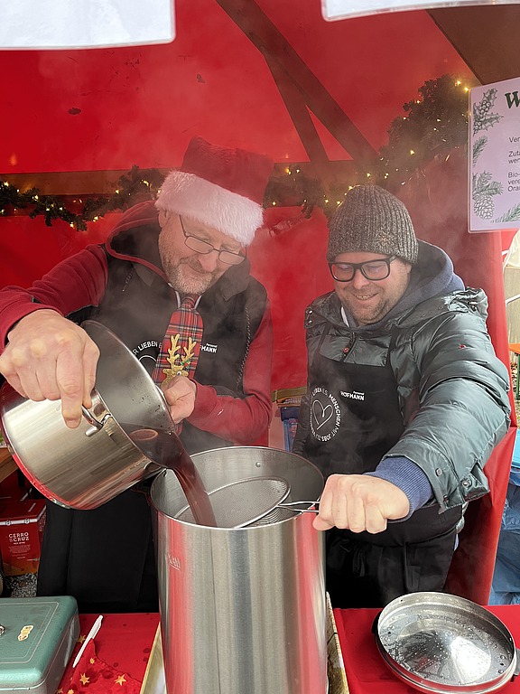 Zwei Mitarbeiter kochen am Stand von Hofmann Personal beim Weihnachtsmarkt Langwasser.