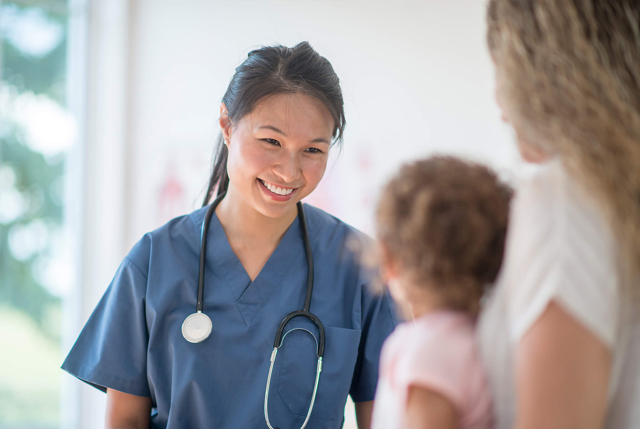 Pflegekraft im Gespräch mit Mutter und Kleinkind, symbolisiert vertrauensvolle Zusammenarbeit im Gesundheits- und Pflegebereich bei medcareer