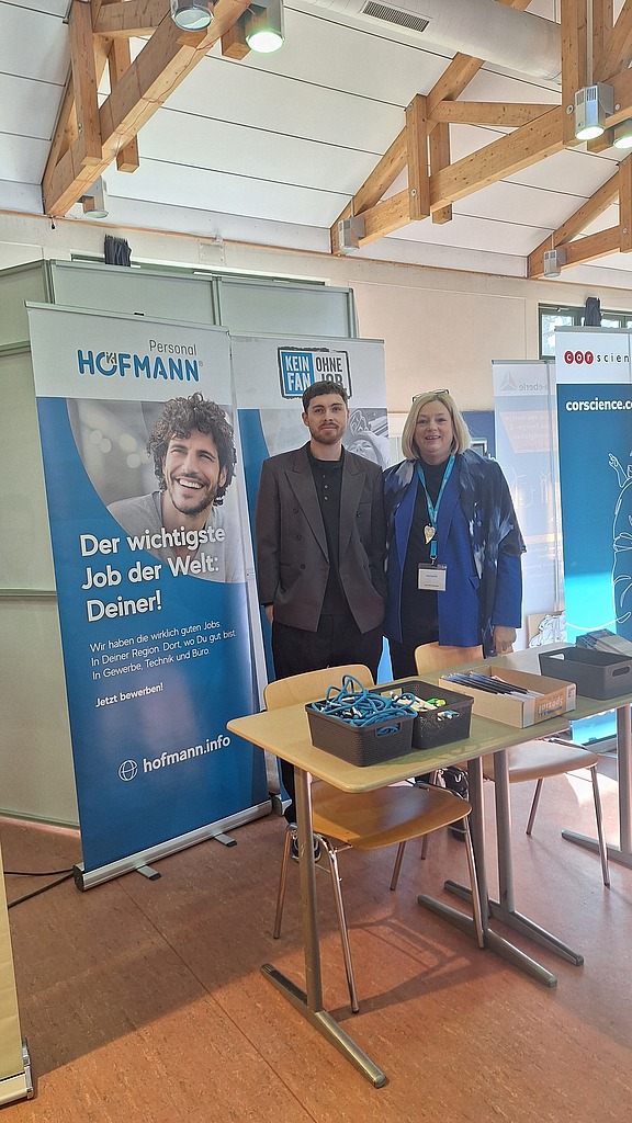 Zwei Mitarbeiter stehen vor dem Messestand von Hofmann Personal beim Tag der Technik 2026 in Erlangen.