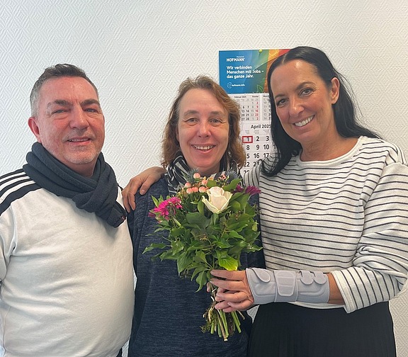 Einer Frau im blauen Pullover werden Blumen überreicht, symbolisch für Teamgeist und wertschätzende Kommunikation bei Hofmann Personal.