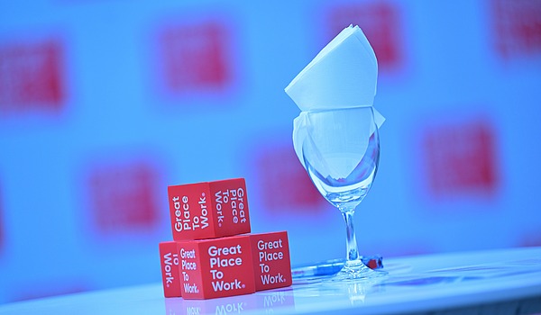 Kleine rote Great-Place-To-Work-Würfel neben einem edlem Glass. 