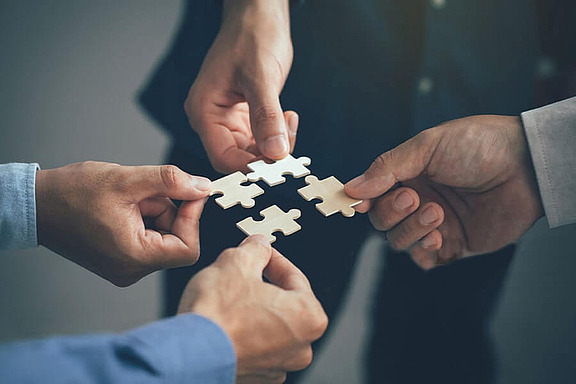 Mehrere Hände setzen Puzzleteile zusammen, symbolisieren Teamarbeit bei hpm (Hofmann Projektmanagement)