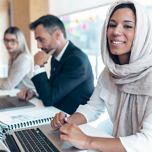 Mitarbeitende unterschiedlicher Herkunft arbeiten gemeinsam an Laptops in einem modernen Büro, Zeitarbeit.