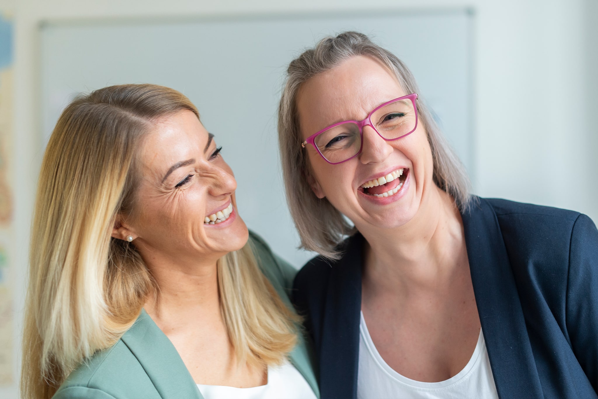 Zwei Kolleginnen lachen gemeinsam, symbolisiert Teamgeist und Zusammenarbeit bei medcareer